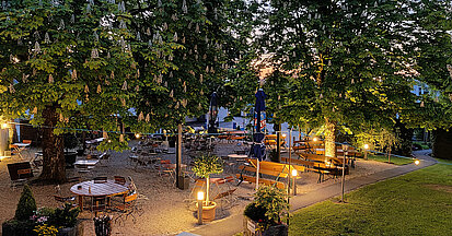 Gemütlich beleuchteter Biergarten mit Kastanienbäumen im Sonnenuntergang - Landgasthof Spetzinger